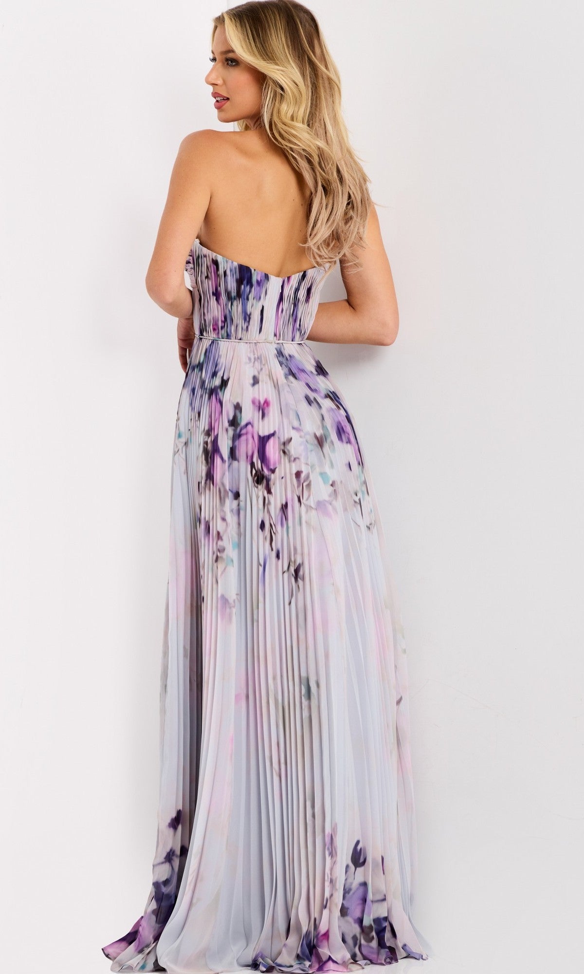 A woman models the Jovani 42564 Long Prom Dress, featuring a strapless floral design in purple and lavender hues, with her back to the camera against a white background.